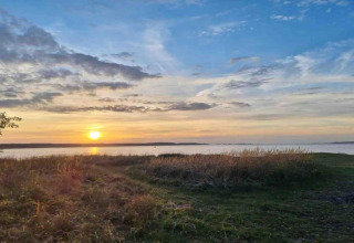 Beautiful sunset over a lake at the Bungalow complex ‘Gänseblümchen 7’ in Germany, featuring grassy shoreline.