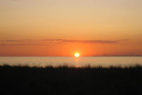 Sunset over the sea as seen from Bungalow complex «Gänseblümchen 7» in Germany, with silhouetted grass.