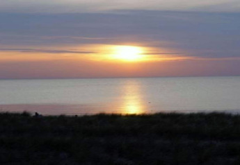 Magnifique coucher de soleil sur la mer vu depuis une cabane, avec des couleurs douces et l'eau calme.