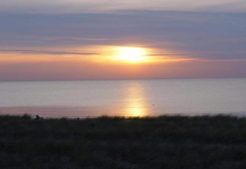 Magnifique coucher de soleil sur la mer vu depuis une cabane, avec des couleurs douces et l'eau calme.