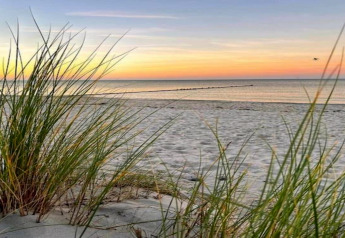 Zonsondergang aan het strand met helmgras, zacht zand en rustige zee bij een glampingaccommodatie.