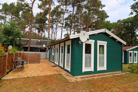 Green wooden cabin with satellite dish, patio, and outdoor seating at Räuberkuhle Koserow, Germany.