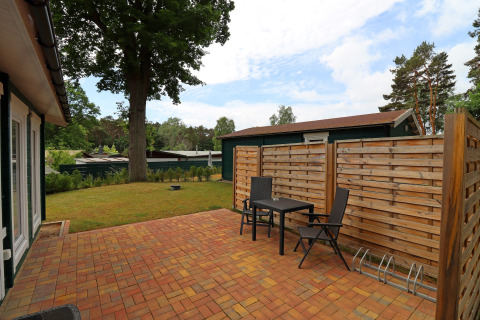 Patio with two chairs and a table by a cabin, wooden privacy fence, and yard in Räuberkuhle Koserow, Germany.