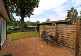 Patio with two chairs and a table by a cabin, wooden privacy fence, and yard in Räuberkuhle Koserow, Germany.