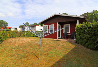 Red cabin with a terrace and rotary clothesline in the garden at Räuberkuhle Koserow, Germany, on a cloudy day.