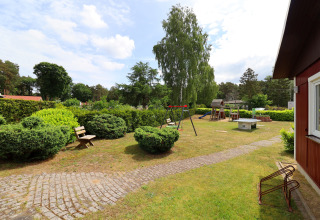 Playground with swings, benches, and greenery in the garden at the Räuberkuhle Koserow cabin, Germany.