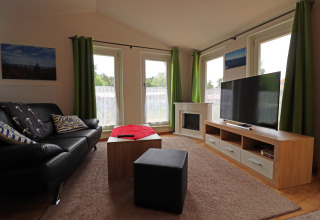 Living room of Räuberkuhle Koserow cabin in Germany with sofa, TV, green curtains and large windows.
