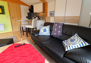 Modern living room at Räuberkuhle Koserow, Germany with a black sofa, nautical pillows, and kitchenette.