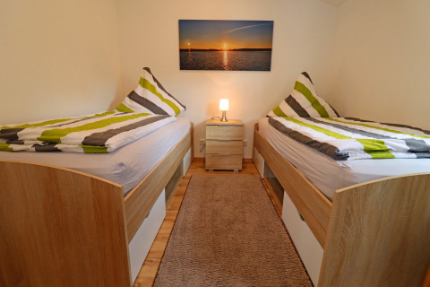 Room at Räuberkuhle Koserow with twin beds, striped duvets, a bedside lamp, and a sunset picture on the wall.