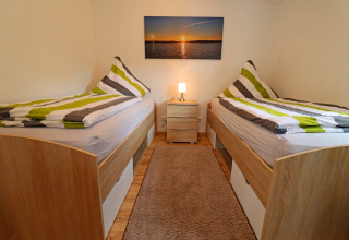 Room at Räuberkuhle Koserow with twin beds, striped duvets, a bedside lamp, and a sunset picture on the wall.