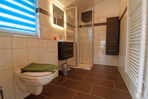 Modern bathroom at Räuberkuhle Koserow, Germany, with shower, toilet, dark cabinets, and tiled floor