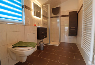 Modern bathroom at Räuberkuhle Koserow, Germany, with shower, toilet, dark cabinets, and tiled floor