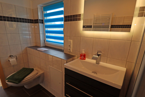 Modern bathroom at Räuberkuhle Koserow cabin in Germany, featuring a wall toilet and illuminated mirror.