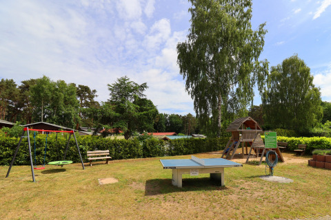 Playground featuring swings, table tennis and a playhouse at Räuberkuhle Koserow cabins in Germany.