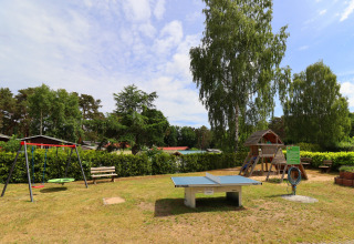Playground featuring swings, table tennis and a playhouse at Räuberkuhle Koserow cabins in Germany.