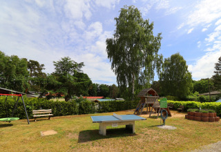 Playground at Räuberkuhle Koserow in Germany featuring ping pong table, swings, and wooden playhouse.