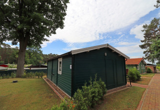 Green wooden cabin at Räuberkuhle Koserow in Germany, surrounded by trees, pathway, and blue sky.