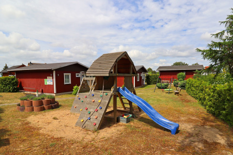 Playground with slide and climbing wall in front of red cabins at Räuberkuhle Koserow, Germany.