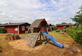 Playground with slide and climbing wall in front of red cabins at Räuberkuhle Koserow, Germany.