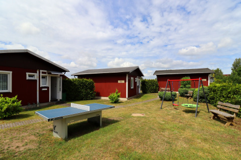 View of cabins at Räuberkuhle Koserow in Germany, featuring a ping pong table and swings outside.