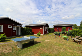 View of cabins at Räuberkuhle Koserow in Germany, featuring a ping pong table and swings outside.