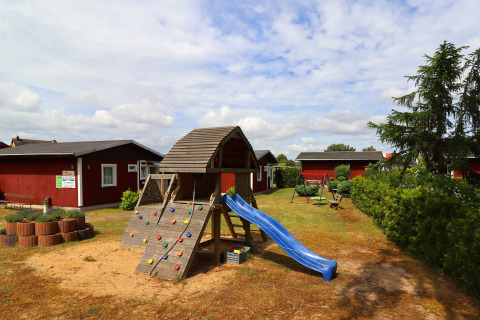 Playground with slide and climbing wall in front of red cabins at Räuberkuhle Koserow, Germany.