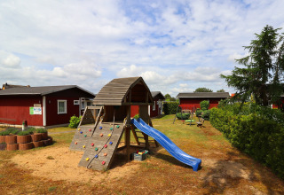 Playground with slide and climbing wall in front of red cabins at Räuberkuhle Koserow, Germany.