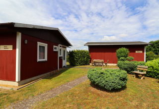 Two red cabins with name signs, benches, and bushes in a garden setting in Räuberkuhle Koserow, Germany.