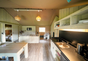 Interieur van een ruime safaritent met moderne keuken, eettafel, zithoek en stapelbedden zichtbaar.