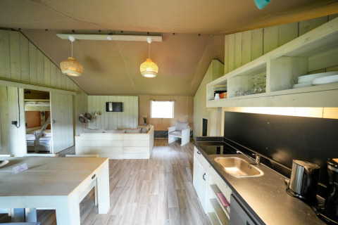 Interior of a spacious safari tent featuring a modern kitchen, dining table, lounge area, and bunk beds.