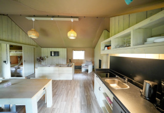 Interior of a spacious safari tent featuring a modern kitchen, dining table, lounge area, and bunk beds.