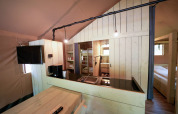 Interieur van een safaritent met houten meubels, kitchenette, stapelbedden en comfortabele slaapkamer.