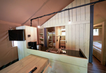 Interieur van een safaritent met houten meubels, kitchenette, stapelbedden en comfortabele slaapkamer.