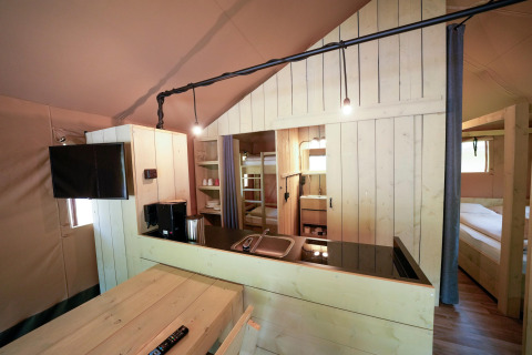 Interior of a safari tent featuring wood furniture, a kitchenette, bunk beds, and a cozy bedroom.