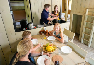 Family enjoys time together in a safari tent, cooking pasta and setting the wooden dining table.