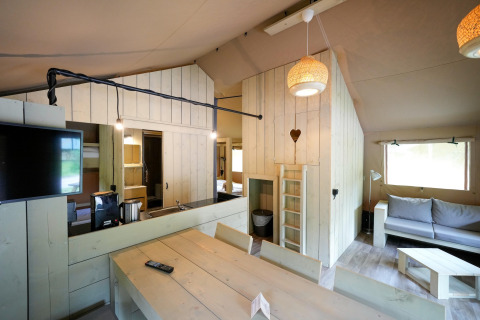 Interior view of a safari tent with modern wooden furniture, cozy lighting, and a sitting area.