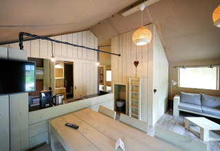 Interior view of a safari tent with modern wooden furniture, cozy lighting, and a sitting area.