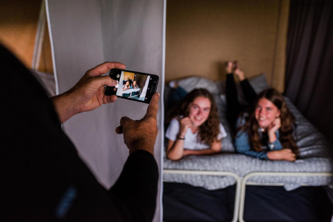 Deux filles souriantes posent sur un lit dans une tente safari pendant qu'une personne prend une photo.
