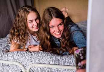 Twee jonge vrouwen liggen op een bed en maken samen een selfie in een safaritent bij Resort Echternacherbrück in Duitsland.