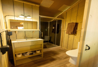 Cozy safari tent bathroom with wooden walls, a shower enclosure, modern sink, towels, and a toilet.