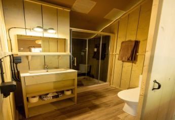 Acogedor baño de tienda safari con paredes de madera, ducha, lavabo moderno, toallas y retrete.