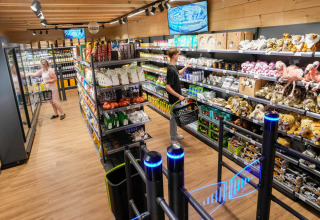 Shopping area in a safari tent with people, shelves of snacks, plush toys, and security monitors.