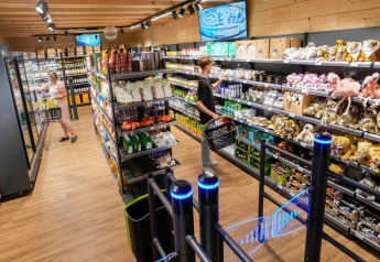 Área de compras en tienda safari con gente, estantes de aperitivos, peluches y cámaras de seguridad.