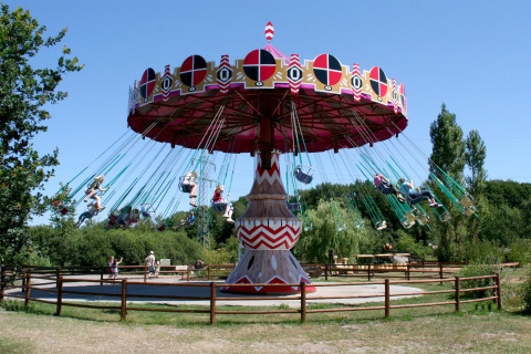 Photo of a colorful swing ride carousel in an amusement park on a sunny day, surrounded by trees.