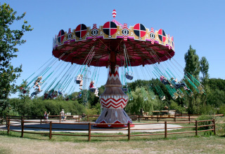 Photo of a colorful swing ride carousel in an amusement park on a sunny day, surrounded by trees.