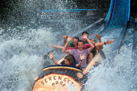 Excited people ride a water log flume, getting splashed at Serengeti Park, with smiles and raised hands.