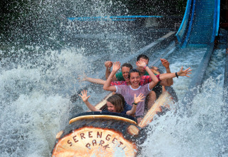 Excited people ride a water log flume, getting splashed at Serengeti Park, with smiles and raised hands.