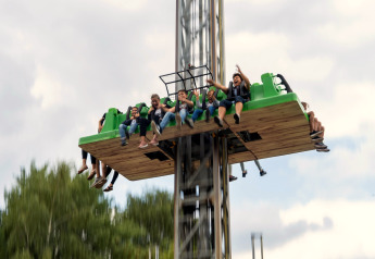Een groep mensen beleeft een spannende vrije val torenrit in een buitenpretpark onder een bewolkte lucht.