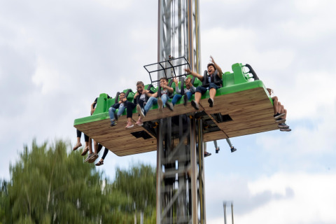 A group of people enjoy an exhilarating drop tower ride in an outdoor amusement park under cloudy skies.