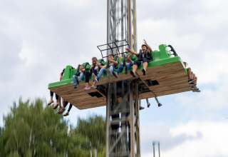 A group of people enjoy an exhilarating drop tower ride in an outdoor amusement park under cloudy skies.